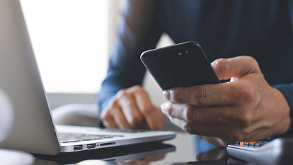 Securepoint Mobile Security with MDM & Firewall to go. A man holds a smartphone in his hand and sits at his laptop