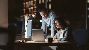 Two people sit together at the computer in the evening