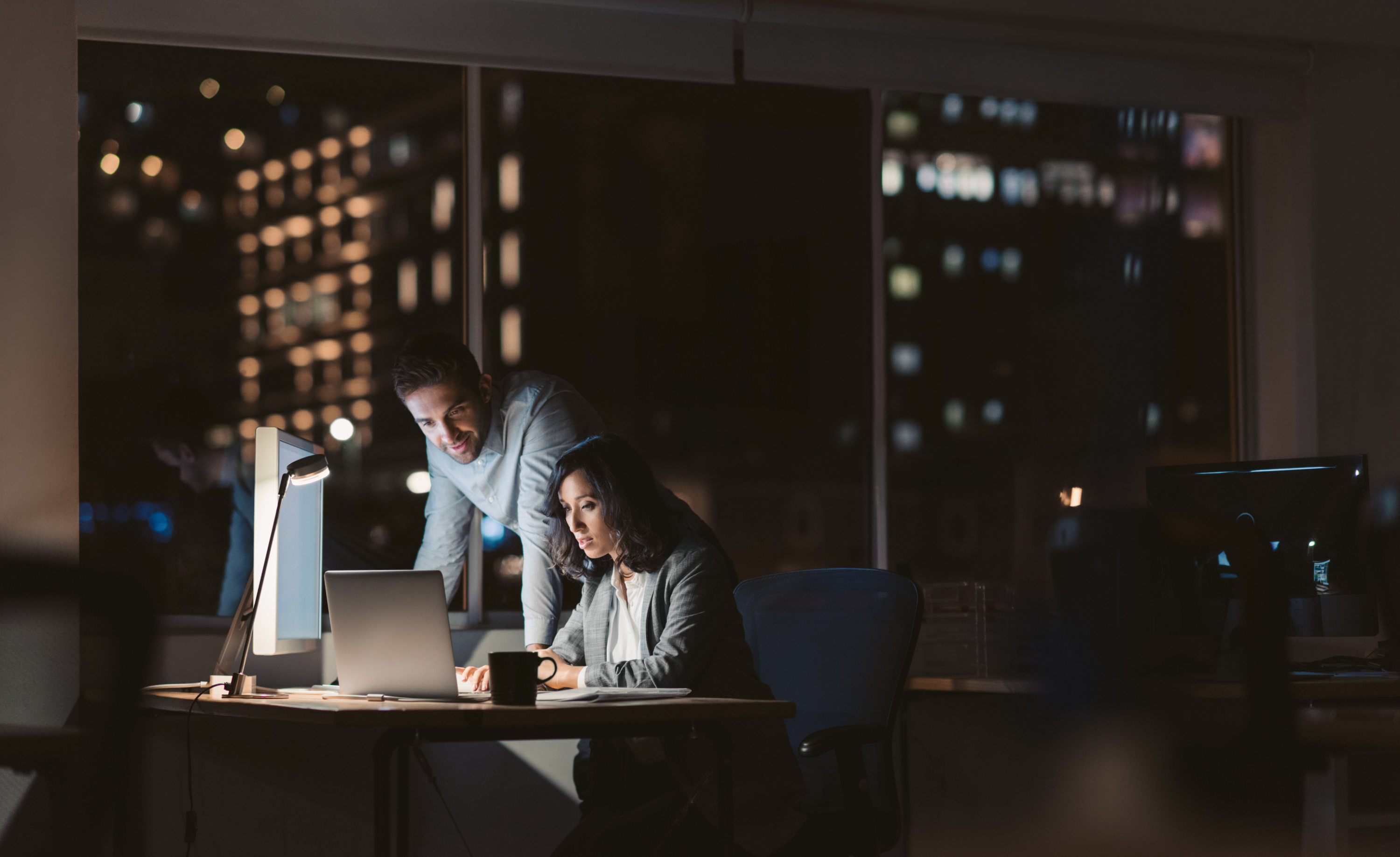 Awareness PLUS as a Service. Man and woman sitting in front of a glowing screen in a dark office