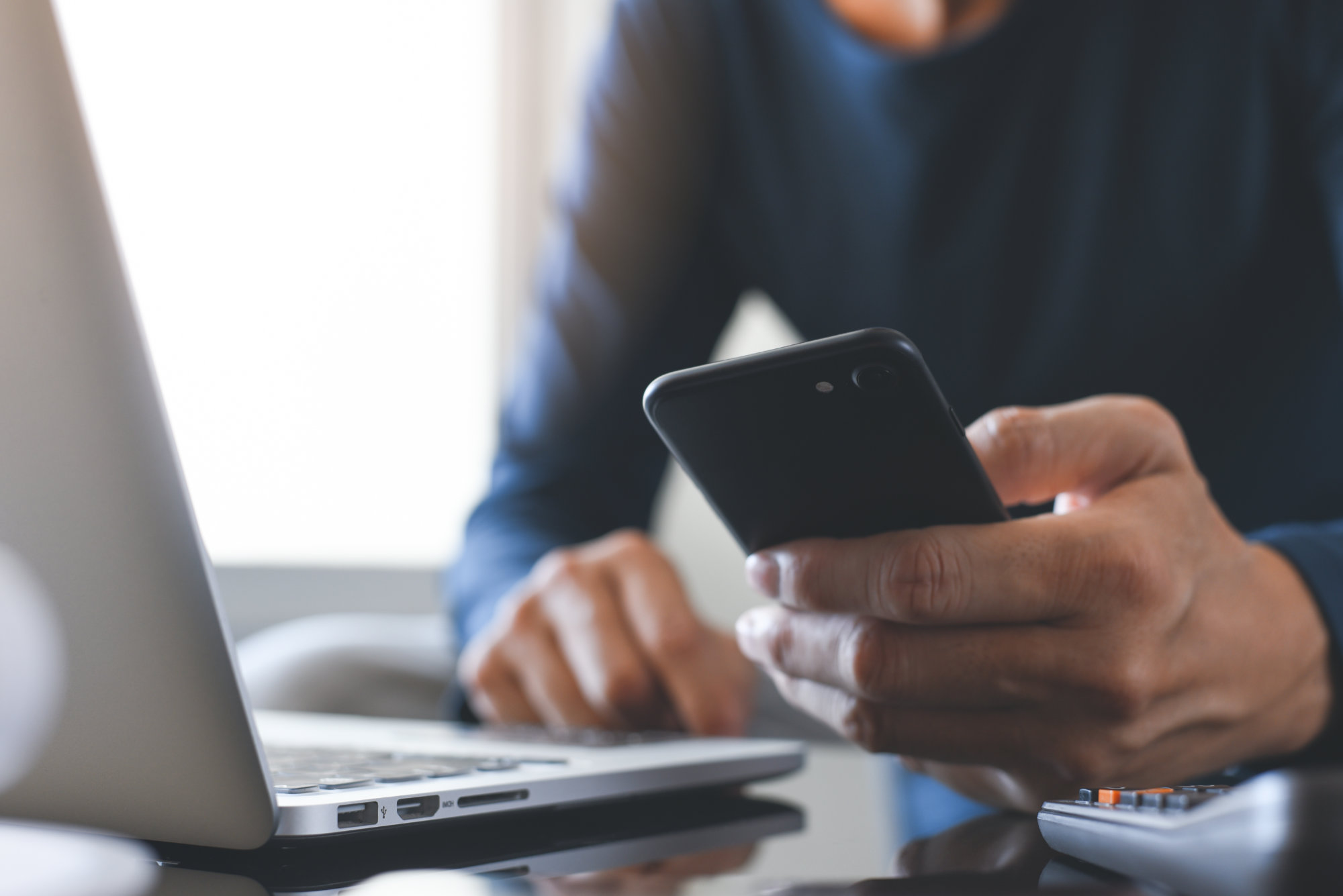 Securepoint Mobile Security as a Service. Man holds smartphone in hand and sits in front of laptop
